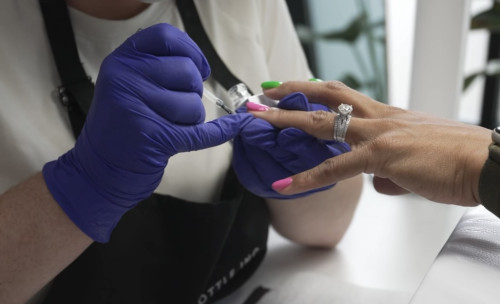 Gloved hands applying gel top coat polish to a pink fingernail